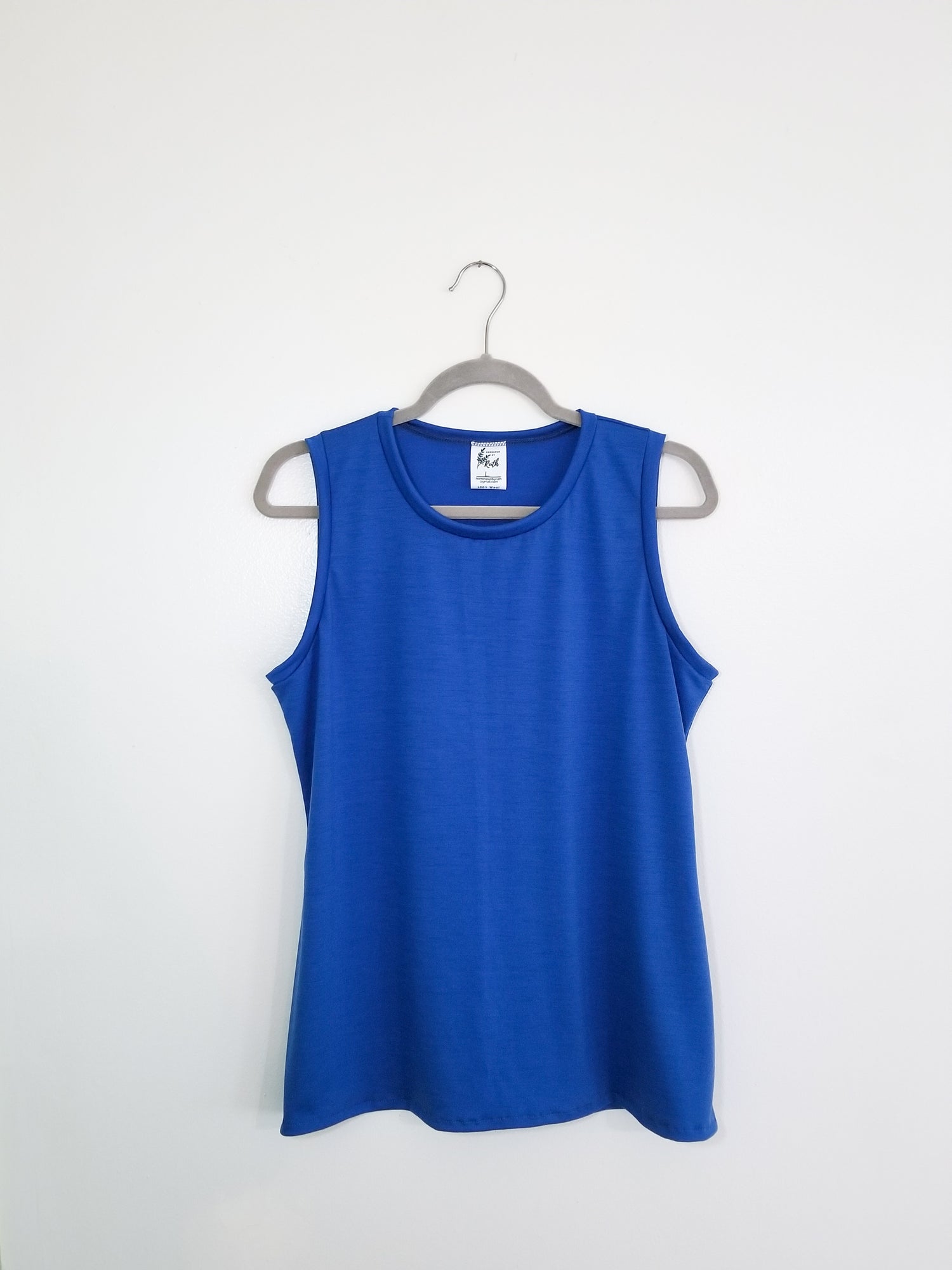 A Blue, 100% Merino wool women's tank top hanging on a grey hanger against a white wall